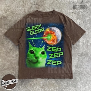 May include: Espresso-colored t-shirt featuring a green alien cat with antennae, a planet being zapped by a green laser, and the words "GLERP! GLORP." and "ZEP ZEP ZEP" in green. The shirt has a vintage, distressed look.