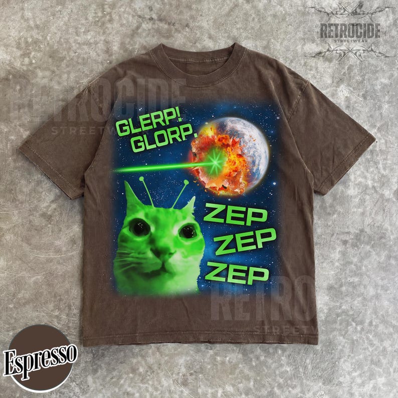 May include: Espresso-colored t-shirt featuring a green alien cat with antennae, a planet being zapped by a green laser, and the words "GLERP! GLORP." and "ZEP ZEP ZEP" in green. The shirt has a vintage, distressed look.