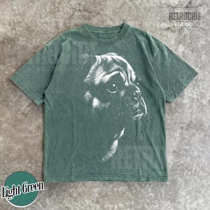 May include: A short-sleeve t-shirt in a muted sage green color featuring a large, detailed white graphic print of a dog's face in profile on the front. The shirt has a crew neckline and a standard fit, with the text RETROCIDE visible in the corner.