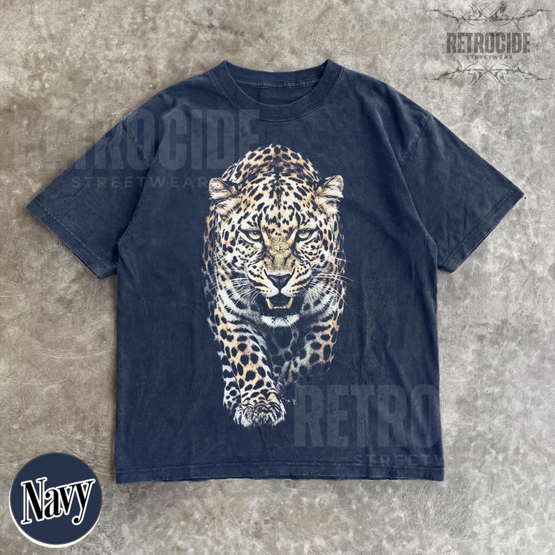May include: Navy blue t-shirt featuring a detailed leopard graphic. The leopard is depicted in shades of brown and black, with a fierce expression. The shirt has a vintage, distressed look, with the word "RETROCIDE" printed on it.