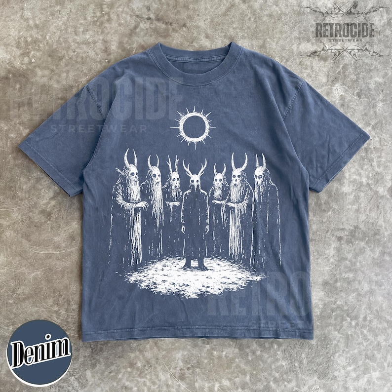 May include: Denim blue t-shirt featuring a white graphic of figures with horned masks and cloaks, under a sun-like symbol. The shirt has the text "RETROCIDE STREETWEAR" and "Denim" in a circle.