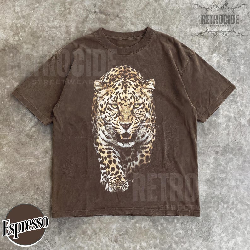 May include: Espresso-colored t-shirt featuring a detailed leopard graphic. The leopard is depicted in shades of brown and tan, with a fierce expression. The shirt has a classic crew neck and short sleeves. The brand name "RETROCIDE STREETWEAR" is printed on the shirt.