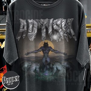 May include: A charcoal gray short-sleeve t-shirt featuring the word AUTISM in a metallic, jagged font across the chest. Below the text is a graphic of a central werewolf standing with arms outstretched before a full moon, flanked by two other wolves.