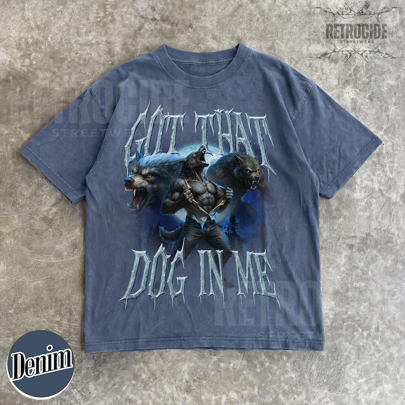 Peut inclure: T-shirt bleu denim avec un motif de loup-garou et le texte "GOT THAT DOG IN ME". Le t-shirt a un col rond et des manches courtes. La marque "RETROCIDE" est imprim&eacute;e en haut.