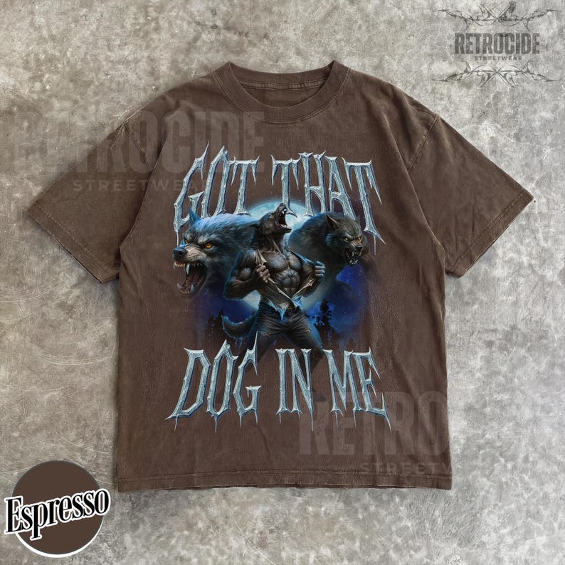 Peut inclure: T-shirt couleur expresso avec un motif de loup-garou et l'inscription "GOT THAT DOG IN ME". Le motif comprend deux loups hurlants. Col rond, manches courtes.