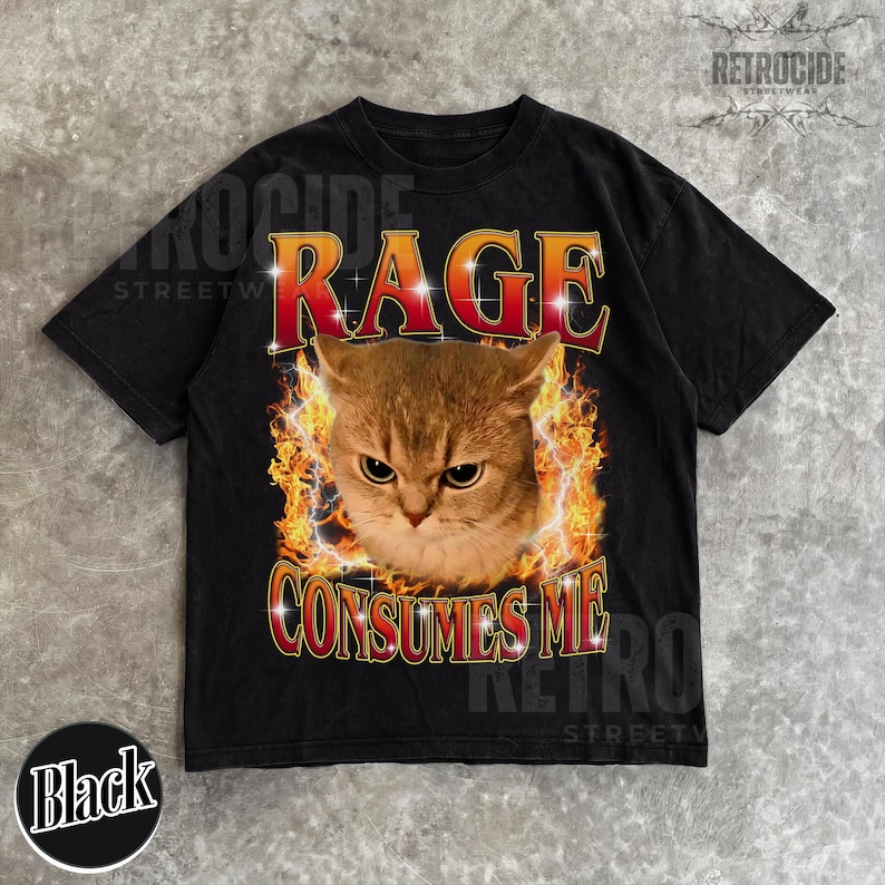 Puede incluir: Una camiseta negra de manga corta con un estampado gr&aacute;fico de una cara de gato rodeada de llamas naranjas y amarillas. El texto RAGE CONSUMES ME est&aacute; impreso en una fuente de degradado rojo y amarillo sobre y debajo de la imagen del gato.