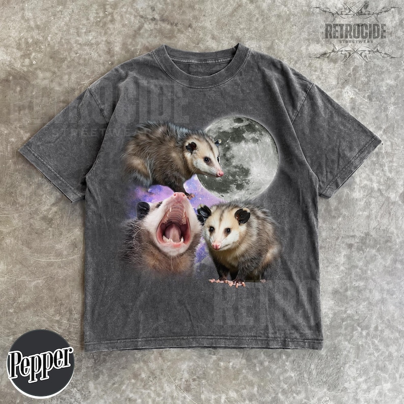 May include: Dark gray t-shirt featuring a graphic of three opossums with a full moon and a galaxy background. The opossums are in various poses, with one yawning. The shirt has a vintage, distressed look.