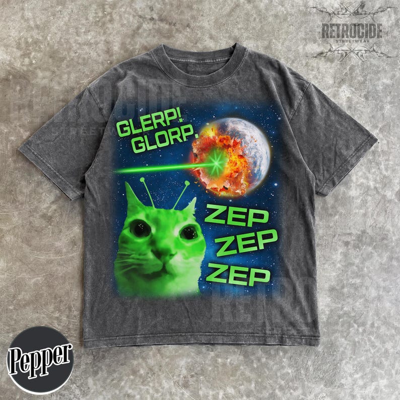 May include: Dark gray t-shirt featuring a green alien cat with antennae, a planet being destroyed by a green laser, and the text "GLERP! GLORP." and "ZEP ZEP ZEP." The shirt has a vintage, distressed look.