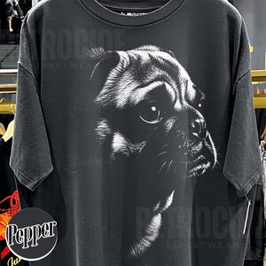 May include: A charcoal gray short-sleeve t-shirt featuring a large, detailed white graphic print of a pug's face on the front. The design captures the dog's expressive eyes and facial features in a high-contrast, sketch-like artistic style.