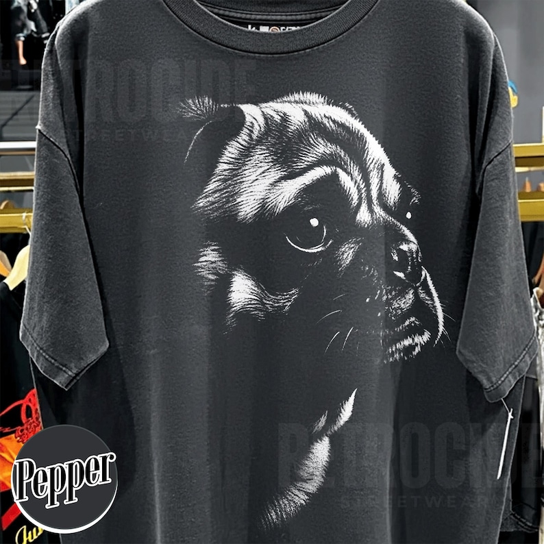 May include: A charcoal gray short-sleeve t-shirt featuring a large, detailed white graphic print of a pug's face on the front. The design captures the dog's expressive eyes and facial features in a high-contrast, sketch-like artistic style.