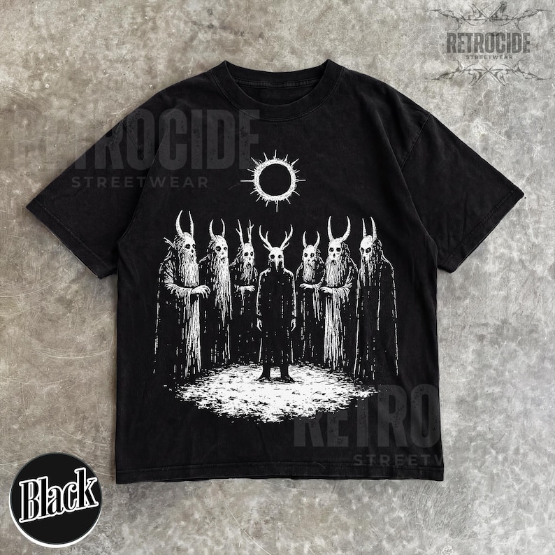 May include: Black t-shirt featuring a white graphic of figures with horned masks and cloaks, standing beneath a sun symbol. The shirt has the text "RETROCIDE STREETWEAR" printed on it. The word "Black" is printed on a black circle.
