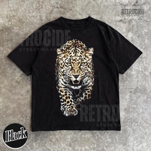May include: Black t-shirt featuring a detailed leopard graphic. The shirt has the text "RETROCIDE STREETWEAR" printed on it. A black circle with the word "Black" is at the bottom. The shirt is made of a soft material.