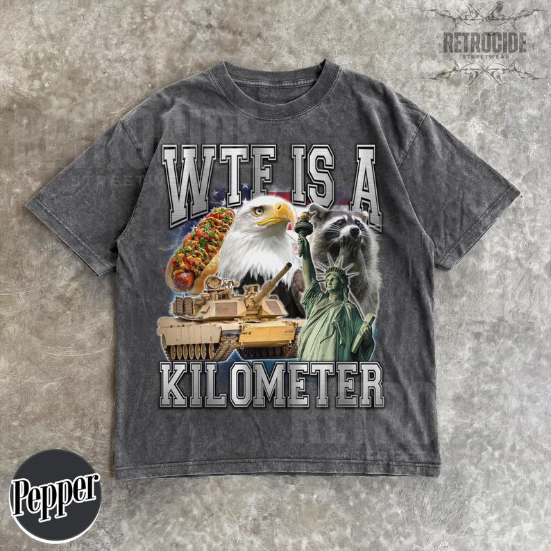 May include: Gray t-shirt with a graphic that reads "WTF IS A KILOMETER." The graphic includes a hot dog, bald eagle, raccoon, tank, and the Statue of Liberty. The shirt has a vintage, distressed look.