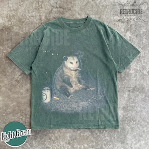 K&ouml;nnte beinhalten: Hellgr&uuml;nes T-Shirt mit einem Aufdruck eines Opossums, das eine Zigarette raucht, mit einer Dose und einem Zigarettenstummel. Das Shirt hat einen Vintage-Look. Der Text "RETROCIDE STREETWEAR" ist oben rechts aufgedruckt.