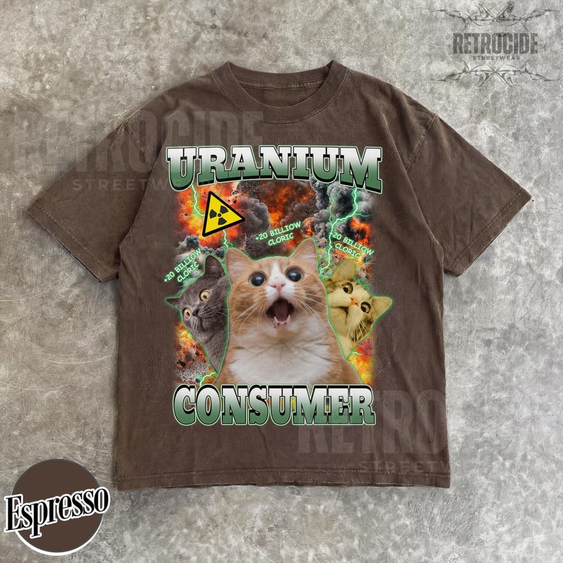 Puede incluir: Una camiseta marr&oacute;n de manga corta con un estampado gr&aacute;fico de tres gatos y el texto "URANIUM CONSUMER" y "20 BILLION CLORIC". El dise&ntilde;o incluye un s&iacute;mbolo de radiaci&oacute;n amarillo, rayos verdes y un fondo de fuego y humo.