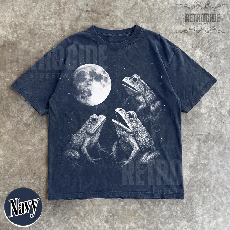 May include: Navy blue t-shirt featuring a detailed illustration of three frogs under a full moon. The graphic is in black and white, with the word "Navy" in a circle at the bottom. The shirt has a vintage, distressed look.