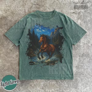 May include: Light green t-shirt with a brown horse graphic running through water, with mountains and trees in the background. The shirt has the text "RETROCIDE" and "Light Green" on it.