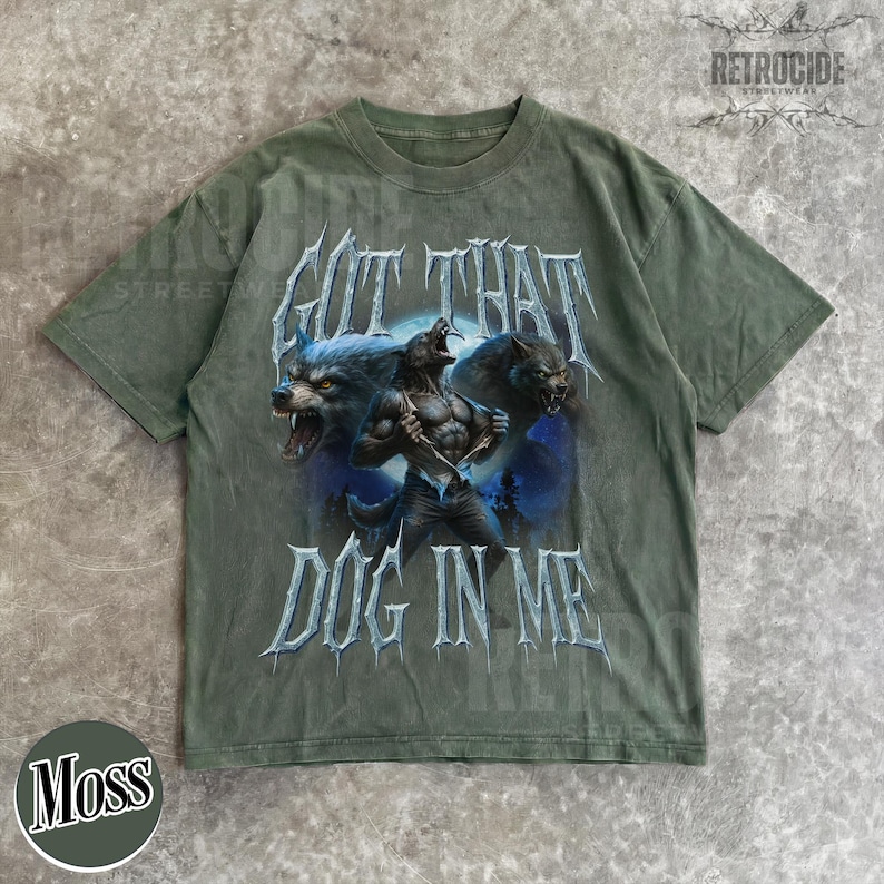 Peut inclure: T-shirt vert mousse avec un motif de loup-garou et le texte "GOT THAT DOG IN ME". Le design pr&eacute;sente trois loups-garous dans des tons bleus et gris. Le t-shirt a un aspect vintage et vieilli.