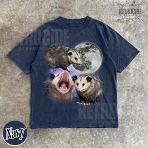 May include: Navy blue t-shirt with a graphic of three opossums, a full moon, and a purple galaxy. The opossums are in various poses, including one yawning. The shirt has a vintage, distressed appearance.