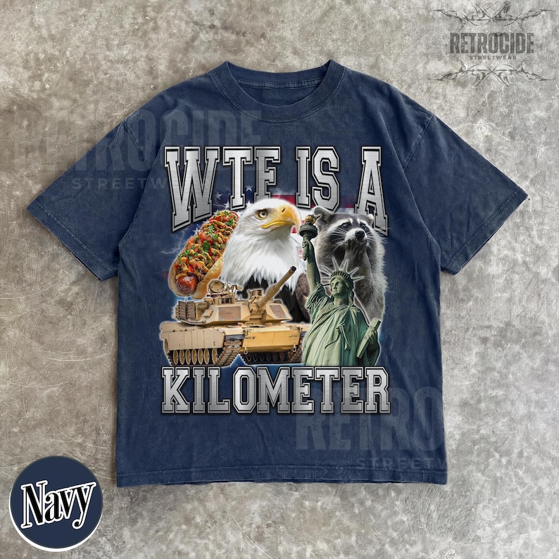 May include: Navy blue t-shirt with a graphic design featuring a hot dog, bald eagle, raccoon, tank, and the Statue of Liberty. The text "WTF IS A KILOMETER" is printed across the front. The shirt has a vintage, distressed look.