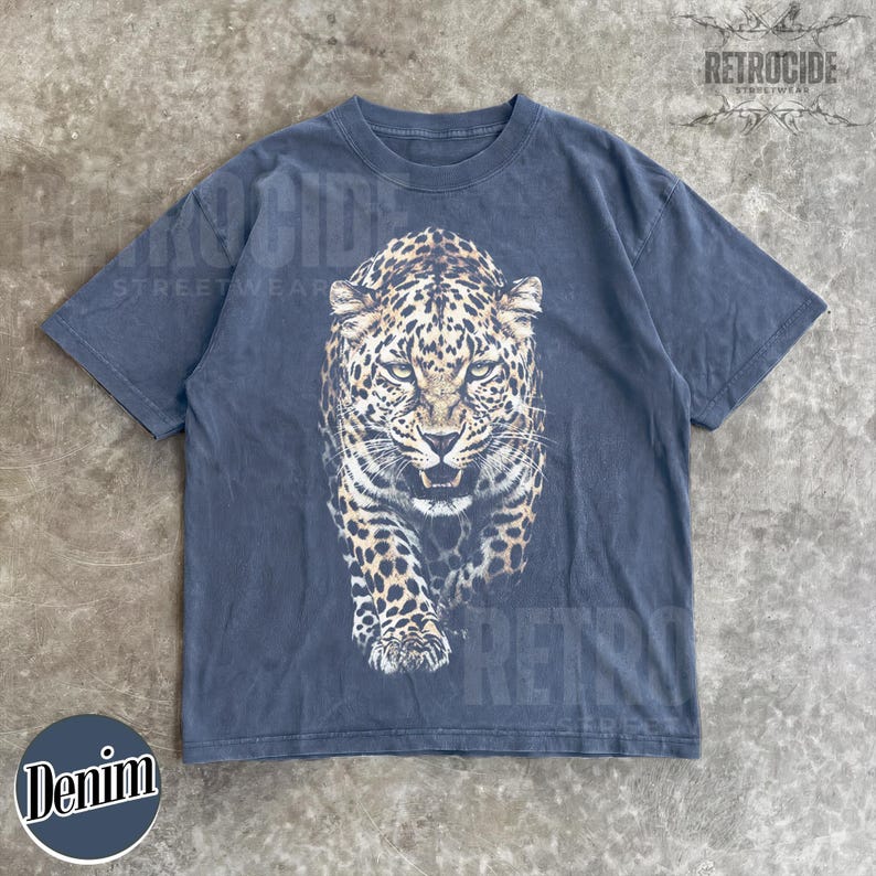 May include: A dark gray t-shirt featuring a detailed leopard graphic on the front. The leopard is depicted in shades of brown, black, and white, with a fierce expression. The shirt has a vintage, washed look and the word "Denim" is printed on the bottom left.