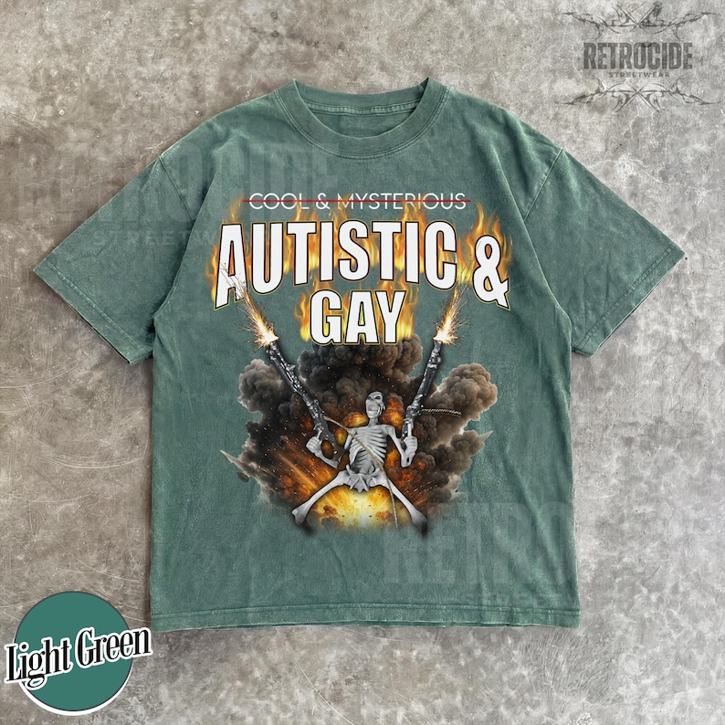May include: Light green t-shirt with the text "COOL & MYSTERIOUS AUTISTIC & GAY" in a bold, stylized font. The graphic features a skeleton figure holding two guns with flames and smoke. The shirt has a vintage, worn look.