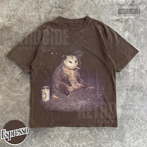 K&ouml;nnte beinhalten: Espressofarbenes T-Shirt mit einer Grafik eines Opossums, das eine Zigarette raucht, mit einer Dose und einem Zigarettenstummel in der N&auml;he. Das Shirt tr&auml;gt den Text "RETROCIDE STREETWEAR".