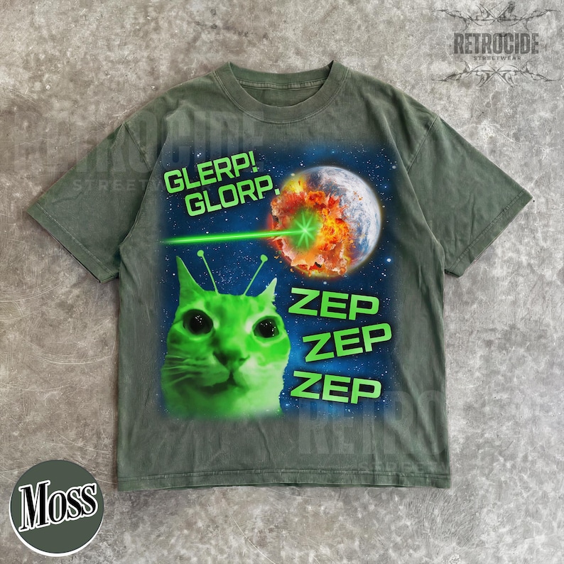 May include: Moss green t-shirt featuring a green alien cat with antennae, a planet being zapped by a green laser, and the phrases "GLERP! GLORP." and "ZEP ZEP ZEP" in neon green. The shirt has a crew neck and short sleeves.