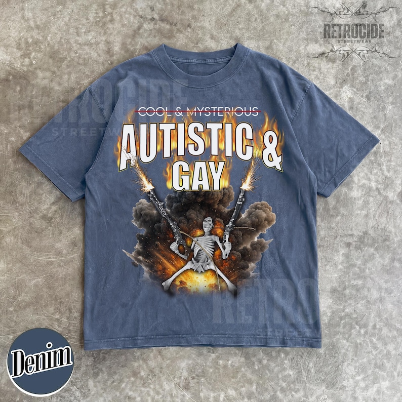 May include: Denim blue t-shirt with the text "COOL & MYSTERIOUS" above "AUTISTIC & GAY" in a bold, white font. A skeleton figure is depicted holding two guns with flames and smoke. The shirt has a vintage streetwear aesthetic.