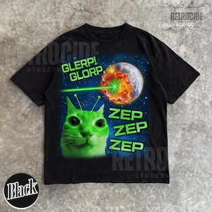 May include: Black t-shirt featuring a green alien cat with antennae, a laser beam, and a planet being destroyed. Text includes "GLERP! GLORP." and "ZEP ZEP ZEP." The shirt has a retro streetwear design.
