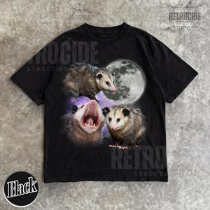 May include: Black t-shirt with a graphic of three opossums and a full moon. The opossums are in different poses, one yawning. The shirt has the text "RETROCIDE STREETWEAR" and "Black" on the bottom.