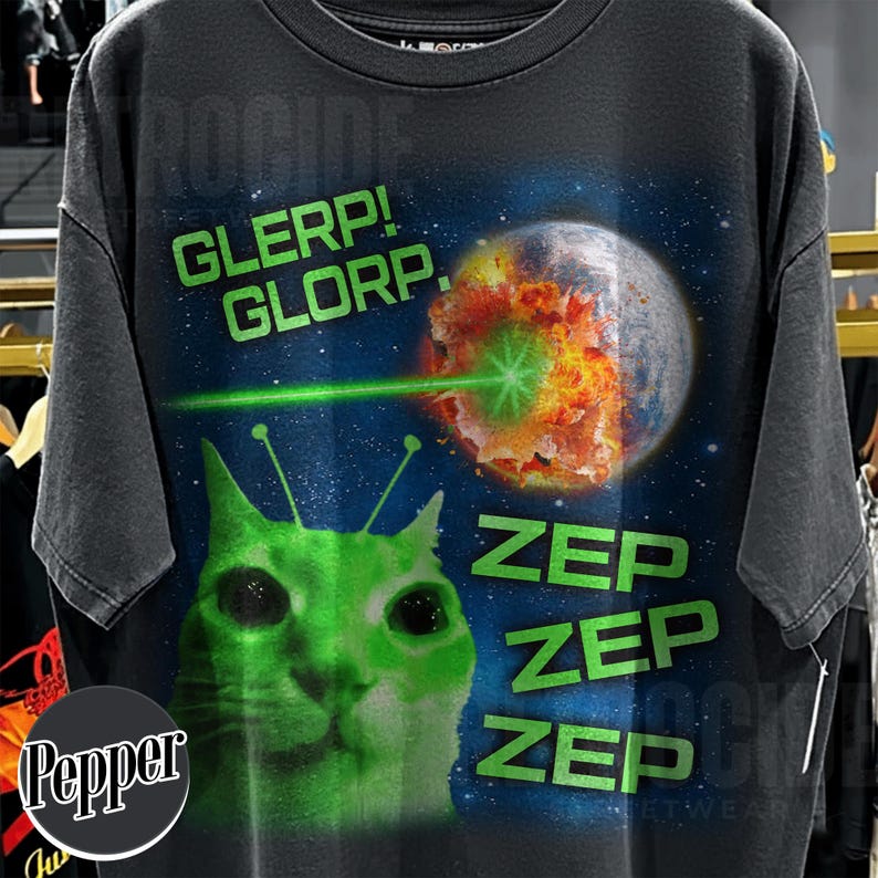 May include: Dark gray t-shirt featuring a green alien cat with antennae, a planet being destroyed by a green laser, and the words "GLERP! GLORP." and "ZEP" in green. The shirt has a vintage, distressed look.