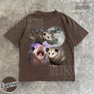 May include: Espresso-coloured t-shirt with a graphic of three opossums and a full moon. The opossums are in various poses, one yawning. The shirt has a vintage, distressed appearance. The word "RETROCIDE" is printed on the shirt.