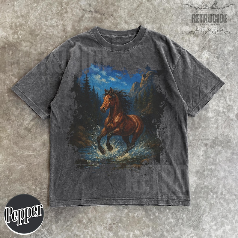 May include: Dark gray t-shirt featuring a brown horse running through water, set against a backdrop of mountains and trees. The graphic has a vintage, distressed look. The shirt has short sleeves and a crew neck.