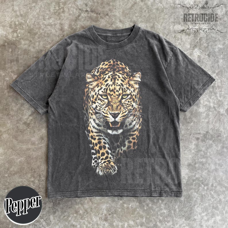 May include: Dark grey t-shirt featuring a detailed leopard graphic. The leopard is depicted in shades of brown, black, and tan, with a fierce expression. The shirt has a vintage, washed-out look. The brand name "RETROCIDE" is printed on the top right.