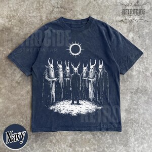 May include: Navy blue t-shirt with a white graphic of figures with horned masks and a sun. The shirt has the text "RETROCIDE STREETWEAR" and the word "Navy" in a circle.