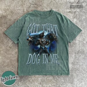 Peut inclure: T-shirt vert clair avec un motif de loup-garou et le texte "GOT THAT DOG IN ME". Le motif pr&eacute;sente trois loups-garous sur un fond bleu et violet. Le t-shirt a un col rond et des manches courtes.