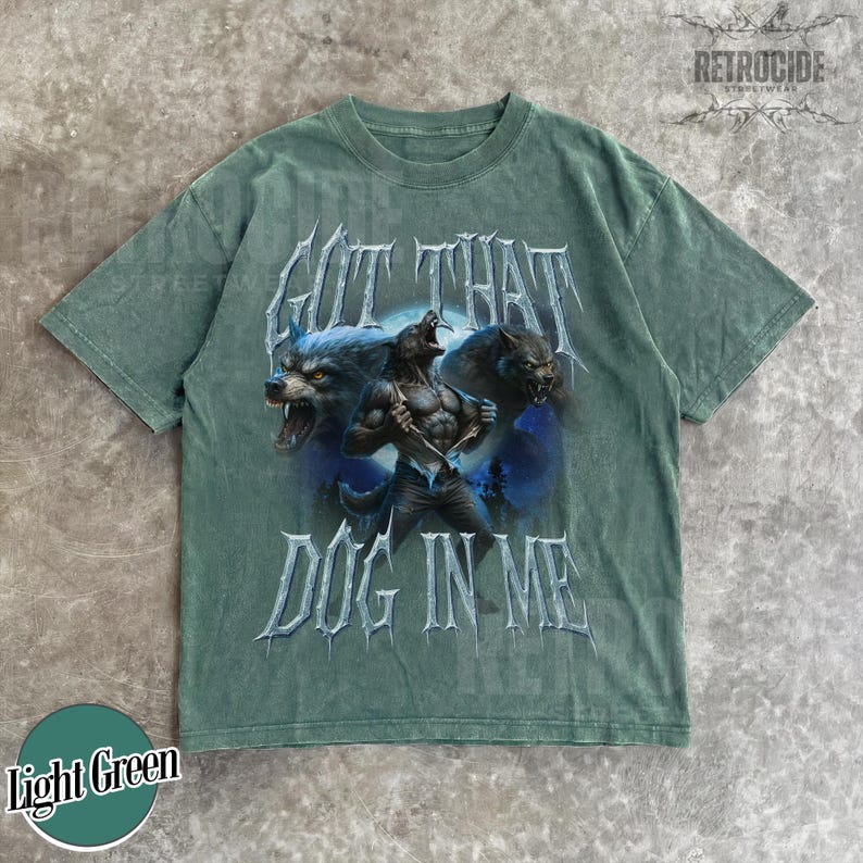 Peut inclure: T-shirt vert clair avec un motif de loup-garou et le texte "GOT THAT DOG IN ME". Le motif pr&eacute;sente trois loups-garous sur un fond bleu et violet. Le t-shirt a un col rond et des manches courtes.