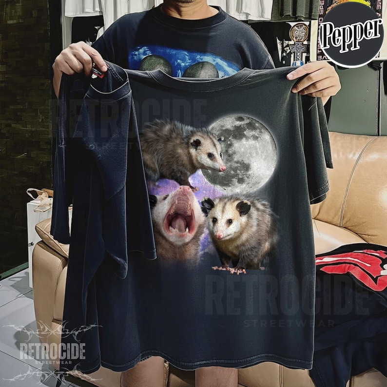 May include: Dark grey t-shirt with a graphic of three opossums and a full moon. The opossums are in different poses, one with its mouth open. The shirt has the text "RETROCIDE STREETWEAR".