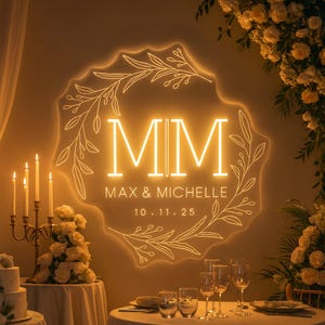 Puede incluir: Un letrero de neón brillante con las iniciales "MM", los nombres "MAX & MICHELLE" y la fecha "10.11.25". El letrero está rodeado por un diseño floral. Un candelabro y flores están en primer plano.
