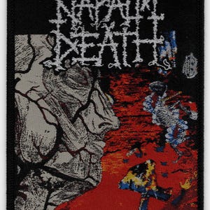 May include: Black rectangular patch featuring the band name "NAPALM DEATH" in white, stylized lettering. The patch has a graphic of a face and a red and blue background. The text "HARMONY CORRUPTION" is at the bottom.