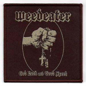 May include: A brown woven patch with the band name "Weed Eater" in white embroidered lettering. The patch features a fist holding a rosary with a cross. The text "God Luck and Good Speed" is embroidered in white below the image.