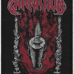 May include: Black patch featuring the word "CARNATION" in red, stylized lettering. The design includes a central, detailed illustration of a cylindrical object with a spiked top, set against a red, fiery background. The text "FATHOMLESS DEPTHS" is at the bottom.