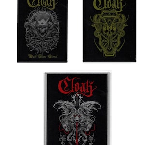 May include: Three black embroidered patches with the word "Cloak" in a gothic font. The patches feature different designs with a skull, a snake, and a creature with wings.