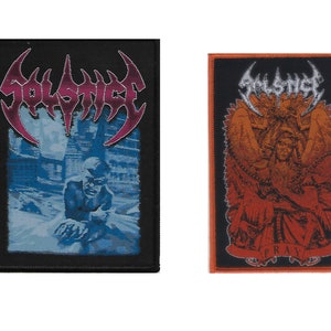May include: Two black and orange embroidered patches. The first patch features the word "SOLSTICE" in a stylized font with a blue and white image of a person in the background. The second patch features a stylized image of an angel with the word "PRAY" at the bottom.