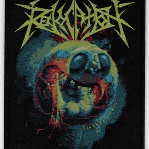 May include: Black patch featuring a skull-like design in shades of blue, red, and yellow, with the text "REALM OF CARCASS" in yellow above the skull. The text "TERRA GENESIS" is written in white along the bottom edge.