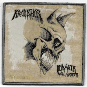 May include: Square patch featuring a detailed illustration of a demonic skull with sharp teeth and horns. The patch has the band name "KRABATHOR" at the top and "DEMONIZER MORTAL MEMORIES II" at the bottom, all in a gothic font. The border is gray.