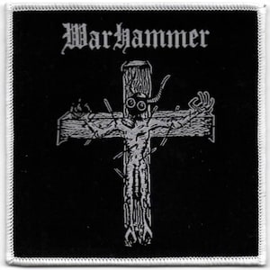 May include: Black square patch with white stitched border. The patch features the word "Warhammer" in gothic font above a white illustration of a figure on a cross. The figure has a mask and outstretched arms.