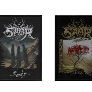 May include: Two black embroidered patches with the band name "SAOR" in white and gold lettering. The left patch features a forest scene with the words "Roots" below. The right patch features a red tree with the words "Aura" below.