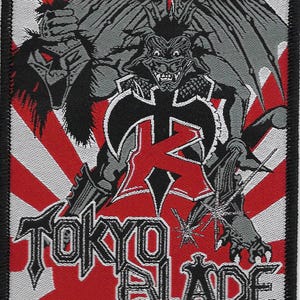 May include: Embroidered patch featuring a demonic figure with wings and a horned head, holding a severed head. The design is set against a red and white background with the text "TOKYO BLADE" in a gothic font.